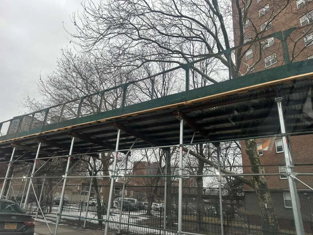 Scaffolding structure elevated above the sidewalk in Queens, NY, offering pedestrian safety while construction work is ongoing on the building above